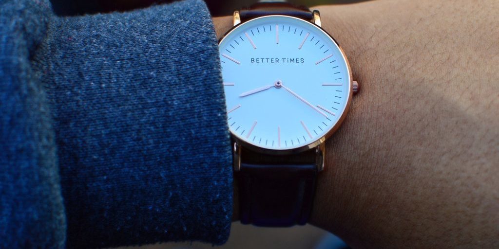 Relógio analógico de pulso com de pulseira escura e visor com fundo branco e aro dourado