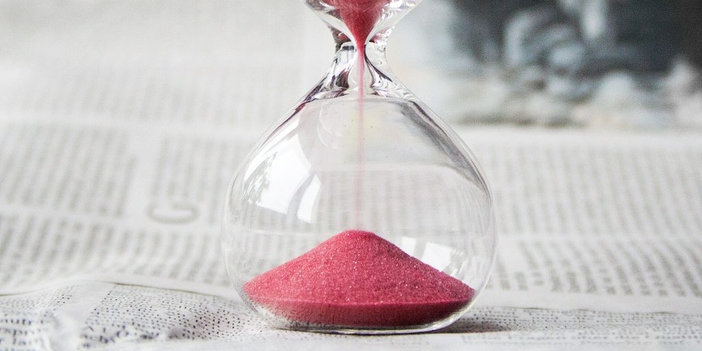 Ampulheta de vidro transparente e areia cor-de-rosa sobre mesa de tampo branca