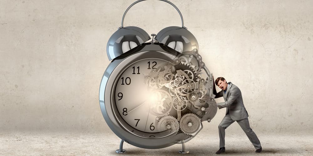 Homem de terno cinza empurrando despertador gigante com engrenagens aparentes