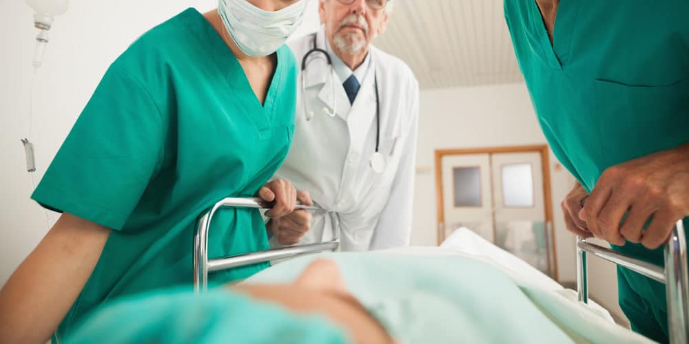 Equipe de médicos e enfermeiros ao redor de uma maca na qual está deitado um paciente em hospital