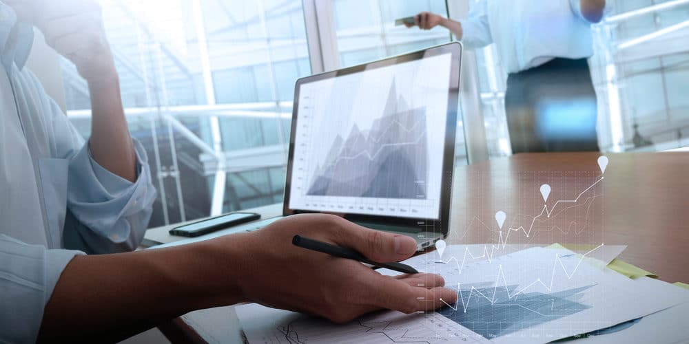 Pessoa analisando gráficos em computador sobre mesa de trabalho em escritório