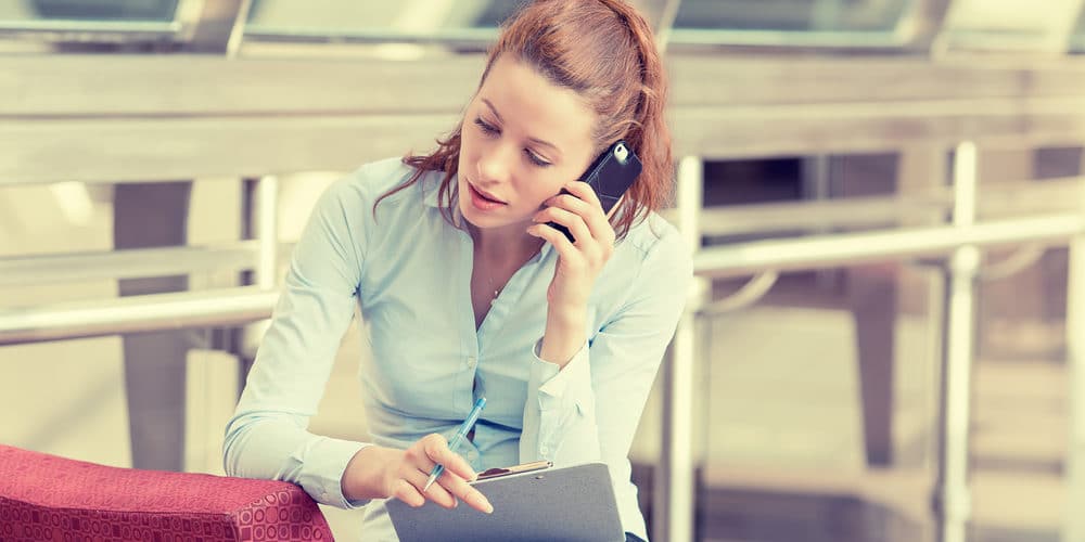 Mulher de cabelos loiros vestida com camisa social fala no telefone em escritório