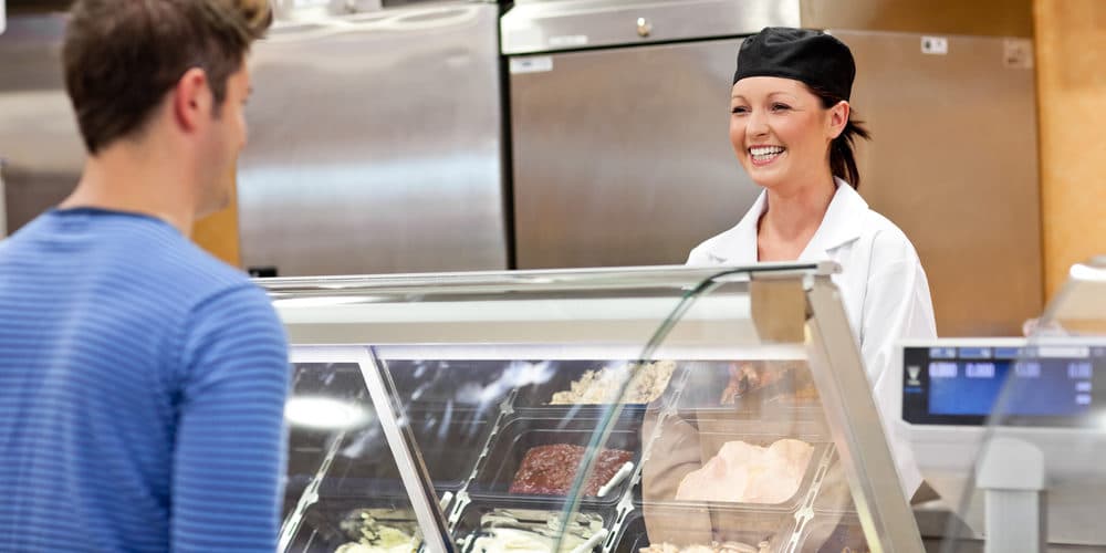 Mulher de cabelos presos e uniforme de lanchonete atendendo cliente no balcão