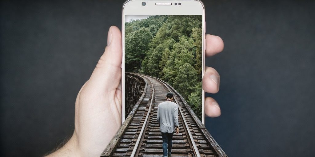 Mão segurando smartphone mostrando uma imagem de uma pessoa andando sobre um trilho de trem
