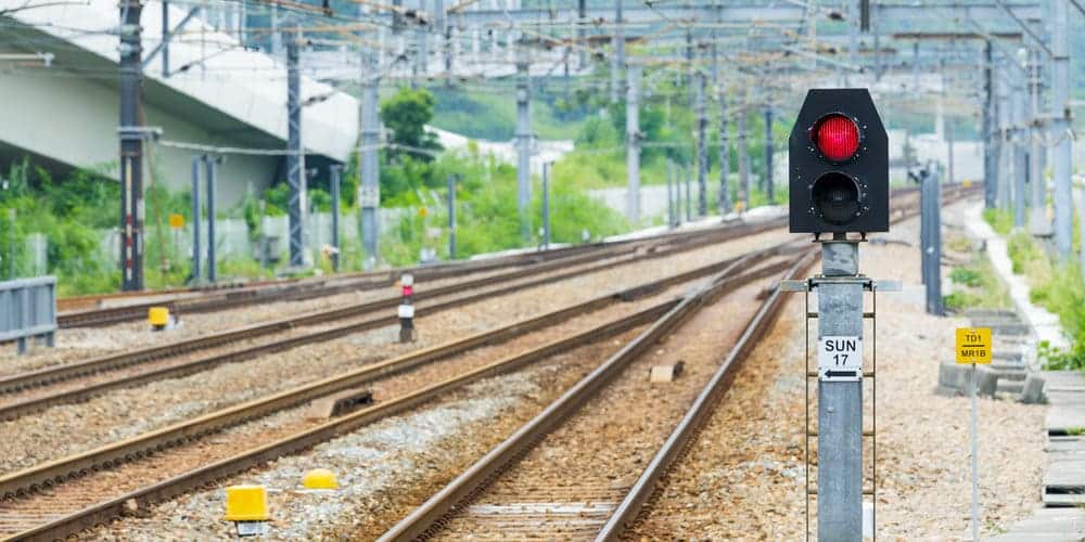 Trilhos de trem vazios em estação, com farol fechado com a luz do semáforo vermelha