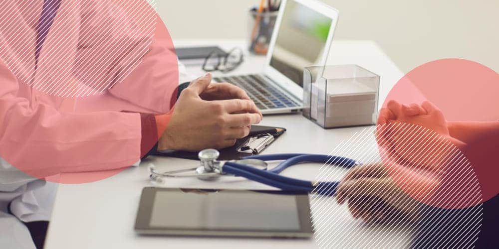 Consultório médico com tablet, computador e estetoscópio sobre mesa clara