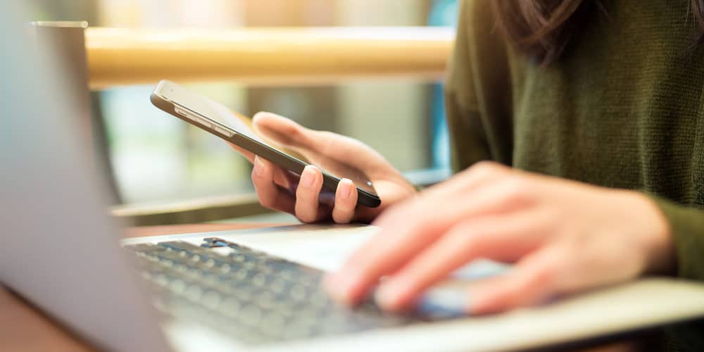 Pessoa trabalhando com seu laptop e smartphone sobre mesa de escritório
