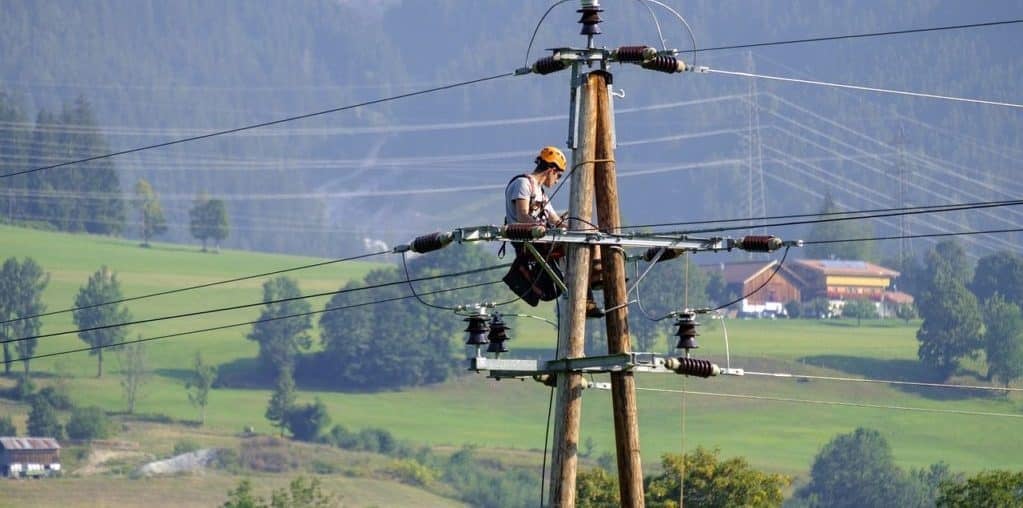 Funcionário de empresa de eletricidade concertando cabos de energia em topo de poste