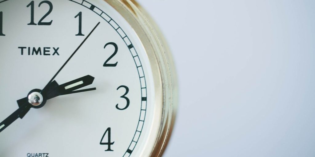 Relógio analógico dourado e branco, pendurado em uma parede branca, marcando as horas com ponteiros