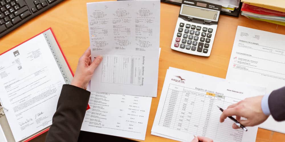 Mesa de contador repleta de documentos fiscais e uma calculadora para calcular a contribuição para o INSS