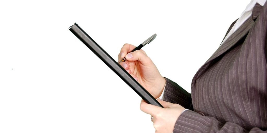 Pessoa fazendo anotações em prancheta com uma caneta preta
