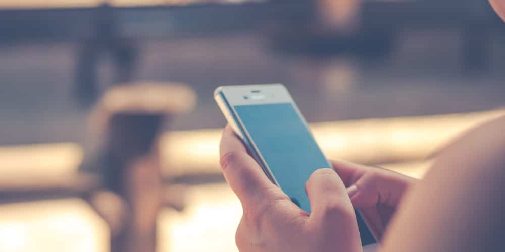 Pessoa manuseando smartphone branco para fazer seu registro de ponto em seu sistema de controle de ponto digital