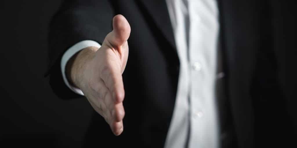 Homem de terno estendendo a mão direita em direção da câmera.