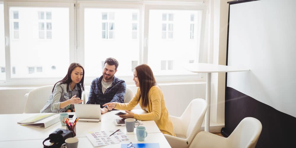 Grupo de colegas de trabalho reunido ao redor de uma ampla mesa em escritório bem iluminado e decorado em cores claras