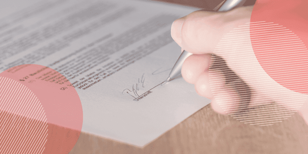 mão em primeiro plano assinando um documento com uma caneta prateada