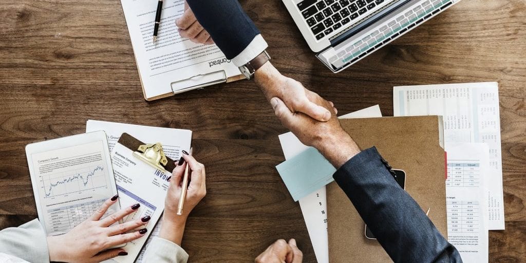 Colegas do RH e Departamento Pessoal apertam as mãos sobre mesa de escritório