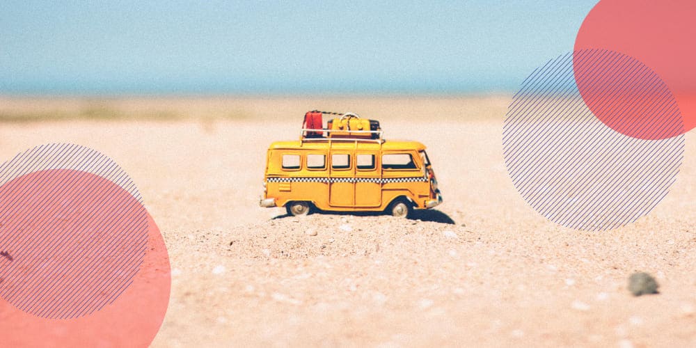 Miniatura de kombi amarela com malas de viagem no teto sobre chão de areia em praia
