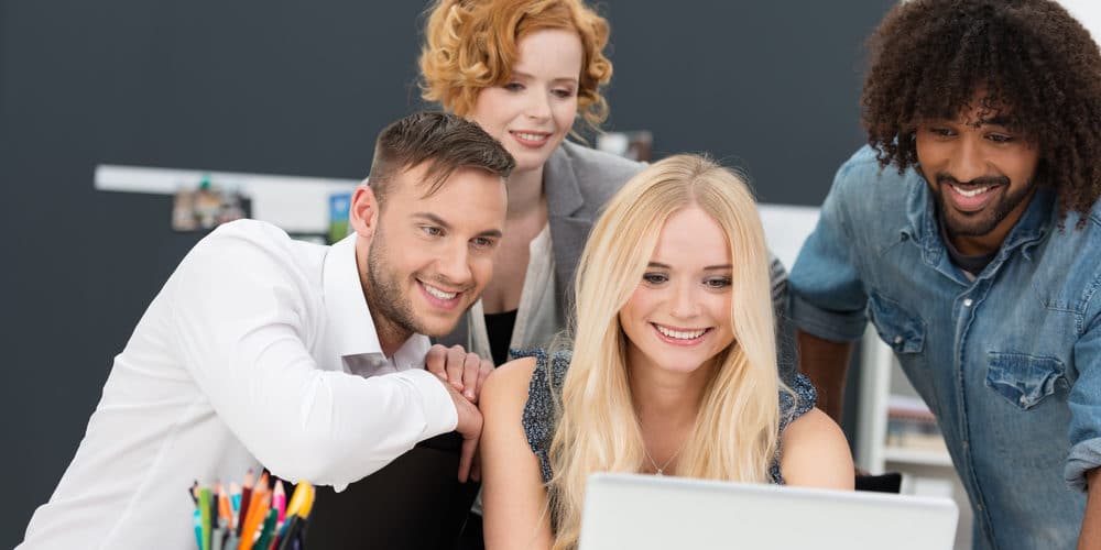 Três mulheres e um homem juntos em frente a um laptop em mesa de escritório