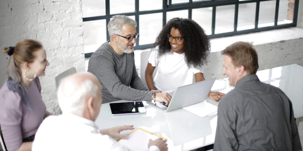 Grupo de quatro colegas de trabalho reunidos em volta de mesa branca em escritório para trabalhar em seus computadores