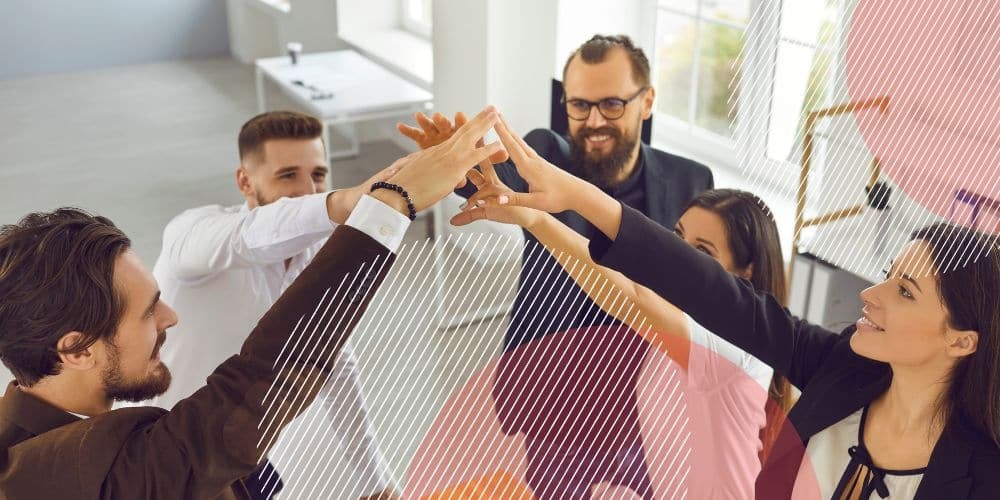 Cinco pessoas unindo as mãos em cumprimento dentro de um escritório bem iluminado