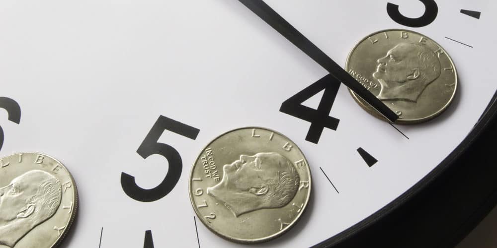 Parte de relógio analógico de ponteiros e números pretos com moedas de prata sobre os números 4 e 5