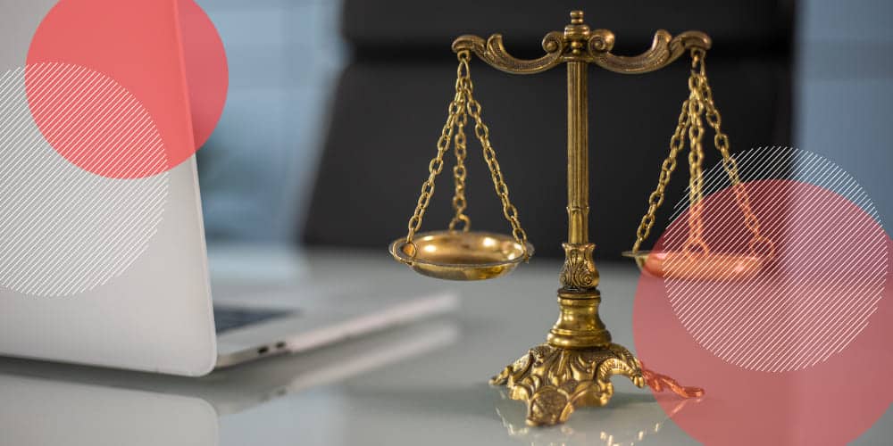 Balança de metal dourado representando a Justiça sobre mesa branca de trabalho ao lado de um computador