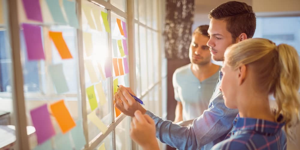 Trio de colegas de trabalho colando post-its coloridos em uma ampla janela em escritório