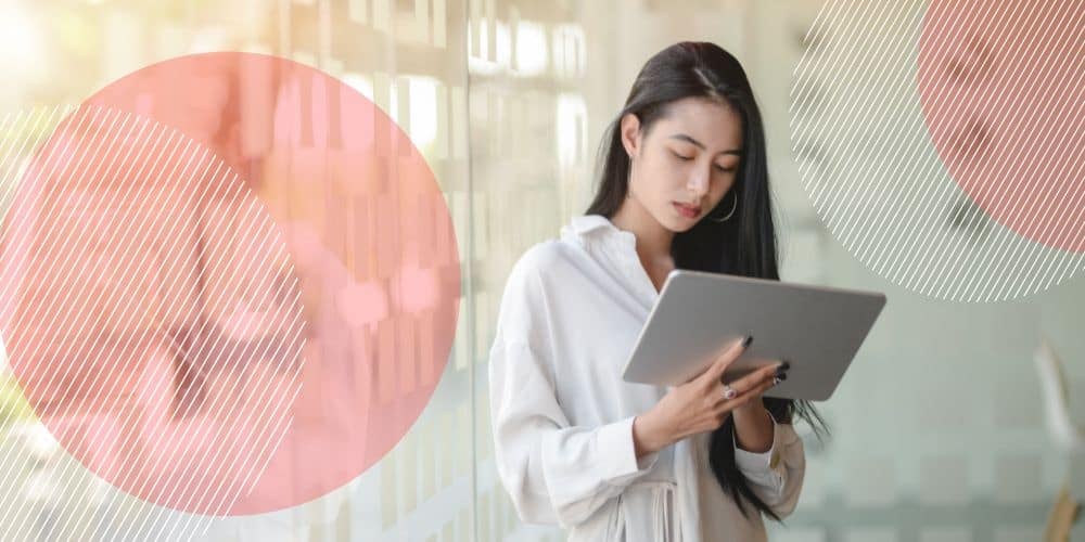 Trabalhadora jovem vestida de branco em um corredor iluminado enquanto mexe num tablet para fazer seu controle de ponto online gratuito