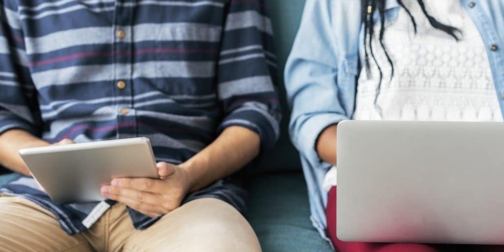 Torsos de um homem e de uma mulher sentados lado a lado enquanto mexem em seus laptops 