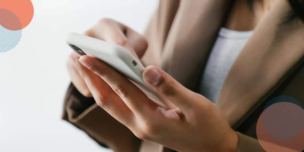 Imagem focada nas mãos de uma pessoa branca que mexe em seu smarphone para bater ponto virtual