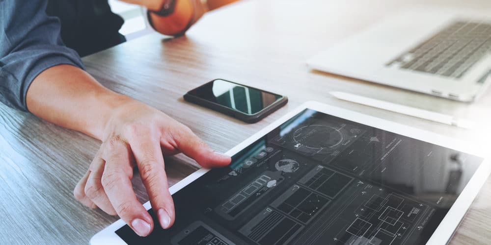 Mãos mexendo em tablet branco e smartphone que estão apoiados sobre mesa de escritório 