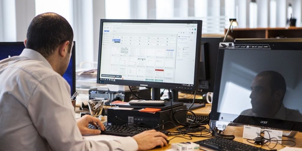 Homem vestindo camisa social de manga longa trabalha em frente a desktop em seu escritório
