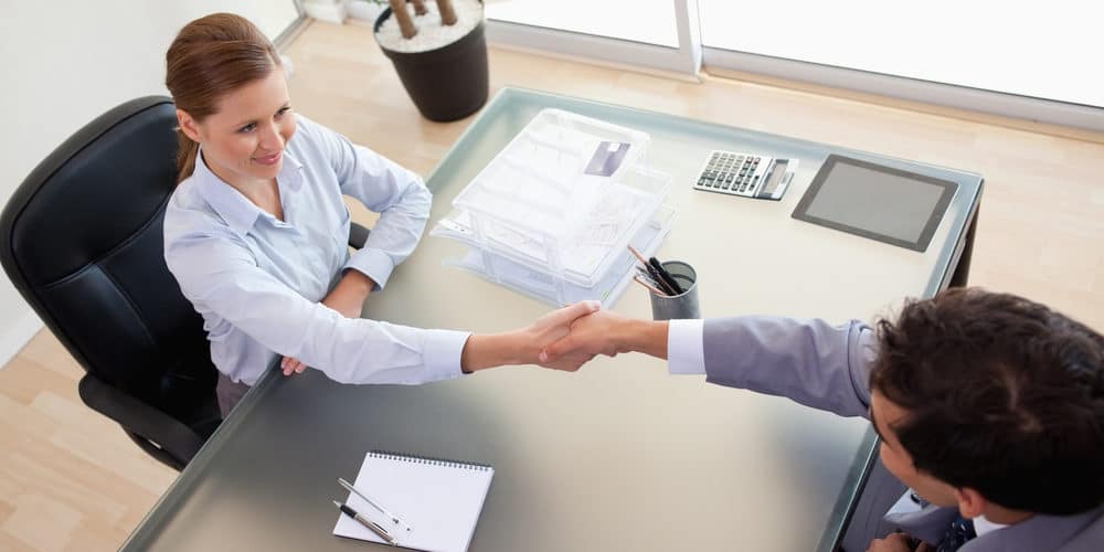 Mulher vestida com roupa social apertando a mão de homem também vestido de roupa social para negociação de readmissão de funcionário