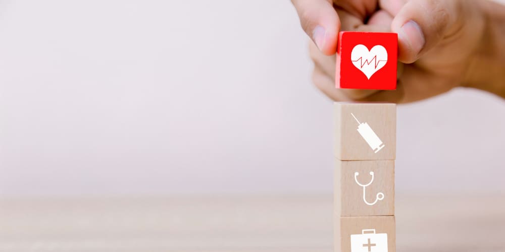 Pecinhas de madeira com desenhos representando coração, estetoscópio e outros itens médicos sendo empilhadas por uma mão