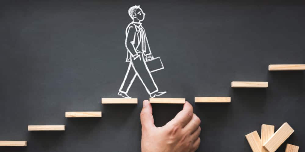 Desenho em giz sobre lousa escura representando um trabalhador subindo pequenos degraus feitos de madeira colados sobre a lousa