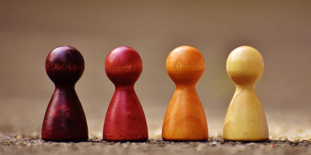 Quatro peças de xadrez nas cores vinho, vermelho, laranja e amarelo enfileiradas lado a lado sobre solo