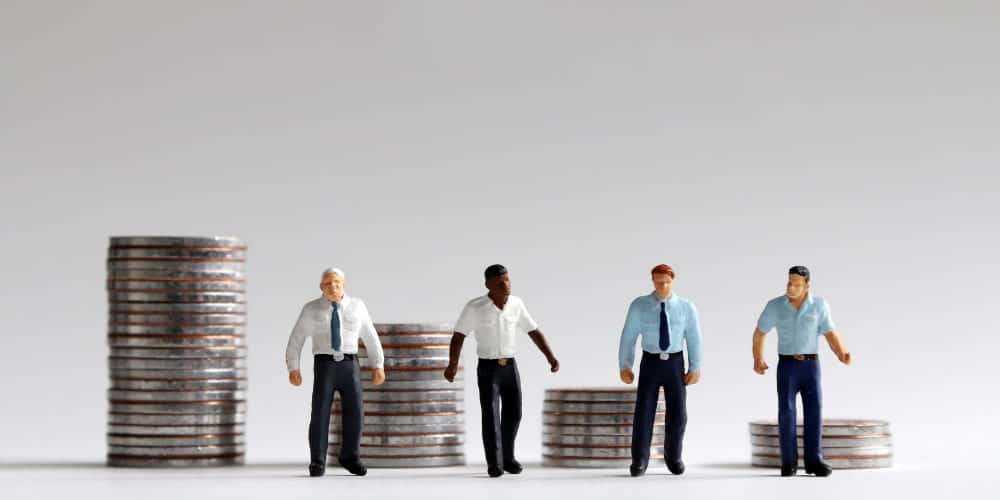 Miniaturas de trabalhadores vestidos com roupas sociais ao lado de pilhas de moedas prateadas