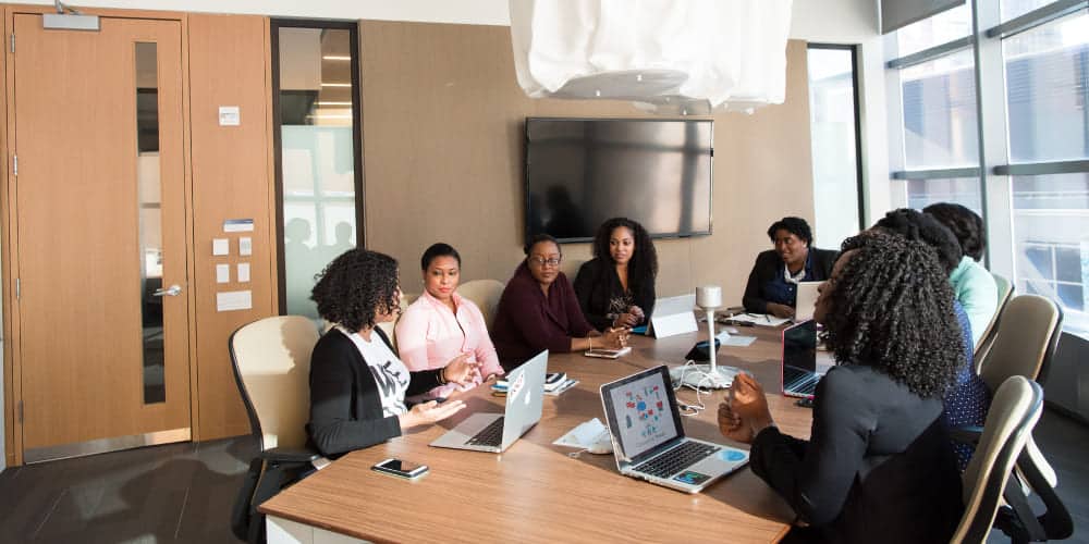 Grupo de profissionais reunidos ao redor de uma mesa redonda em escritório enquanto discutem estratégias de negócio
