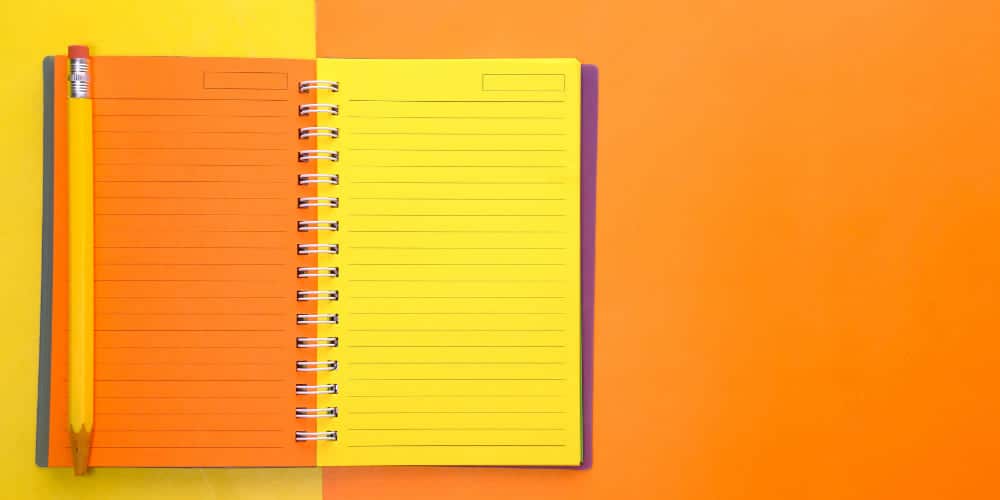 Caderno de folhas amarelas vibrantes apoiado sobre fundo de cartolina laranja intenso