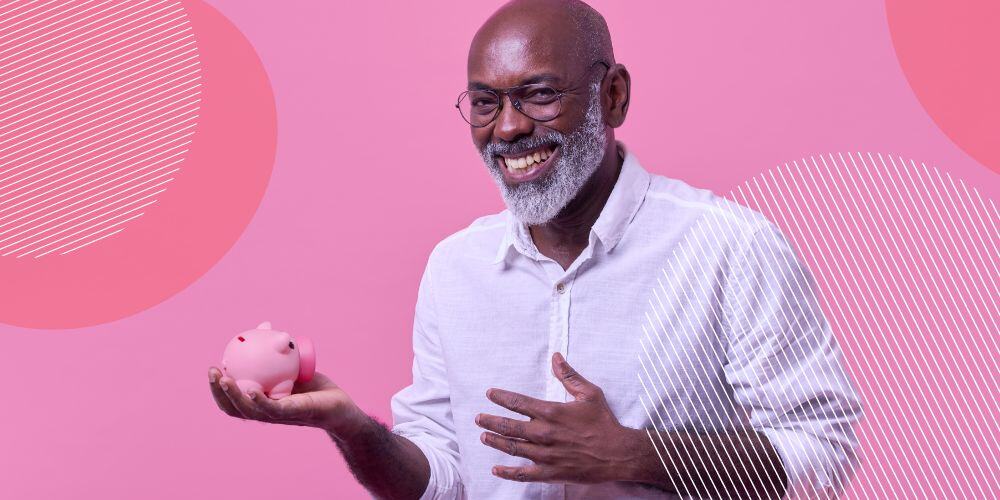 Senhor negro segurando um cofre de porquinho na mão em frente a fundo rosa