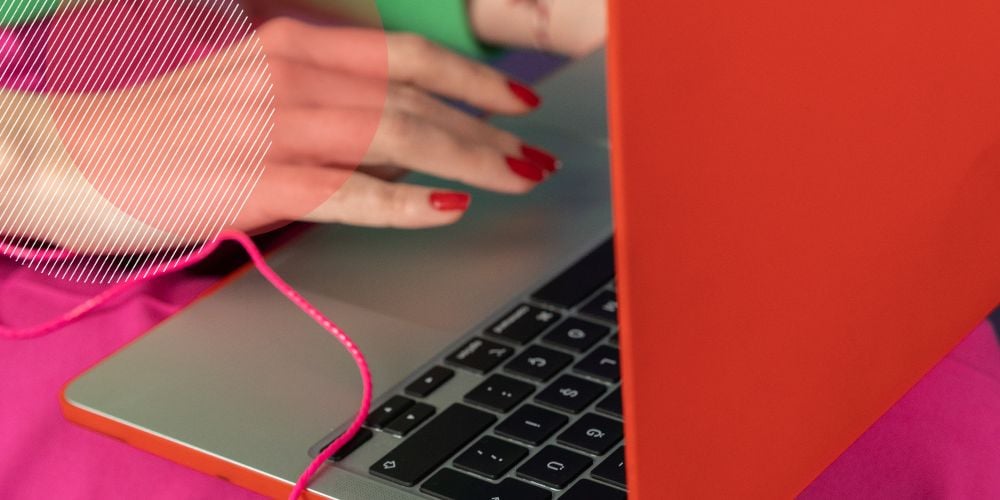 Mão com unhas pintadas de vermelho mexendo em laptop com capa laranja