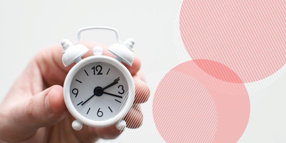 Pequeno relógio analógico branco sendo segurado por uma mão em frente a uma parede branca