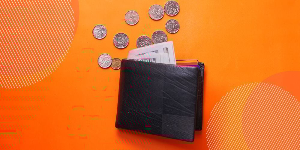 Carteira de couro preto repousada sobre fundo laranja com moedas e notas caindo dela
