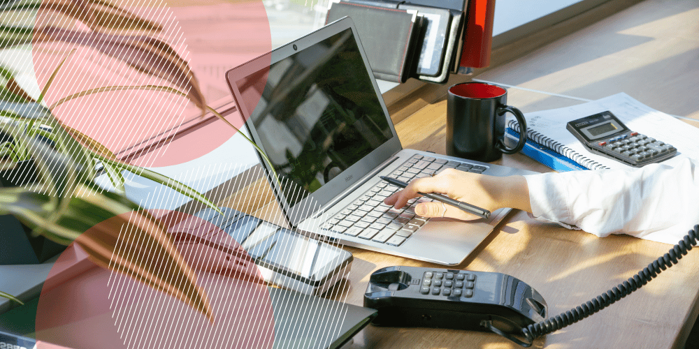 Mesa de trabalho com laptop prateado, xícara de café, plantas e uma máquina de cartão