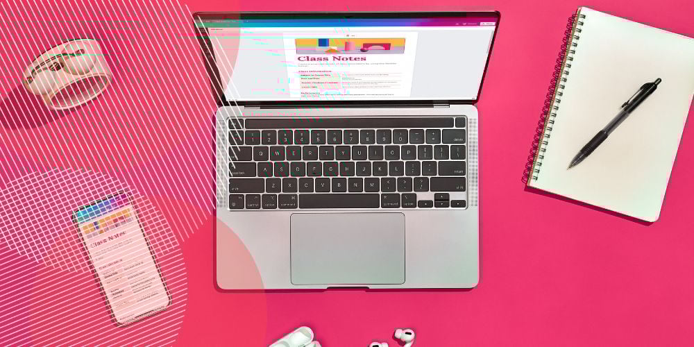 Computador aberto sobre mesa cor-de-rosa com anotações de aula na tela