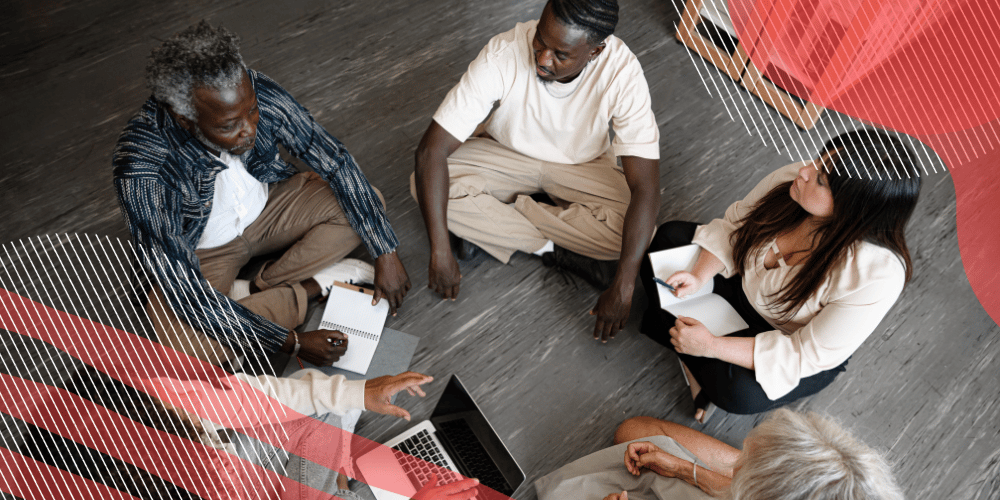 Grupo de cinco colegas de trabalho sentados em círculo no chão para fazerem a avaliação por competências