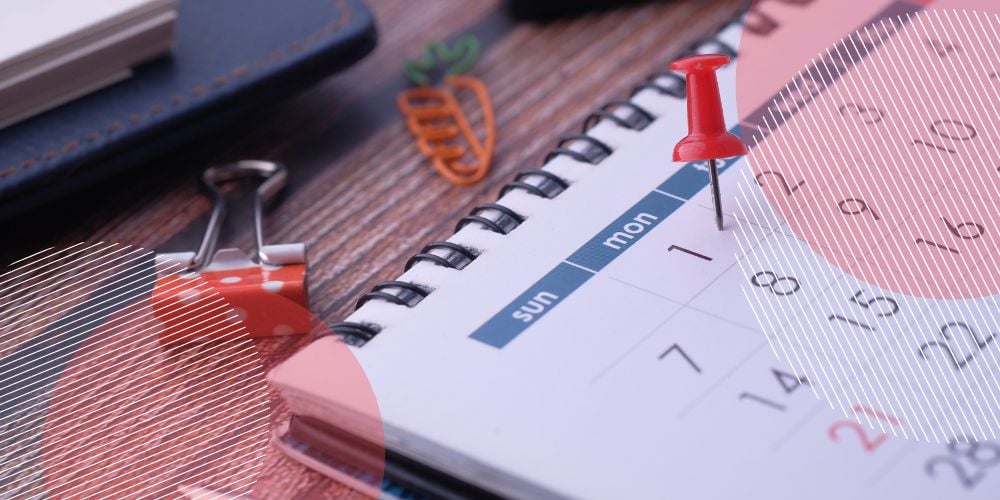 Calendário de papel aberto sobre mesa de madeira com pin vermelho sobre o dia 1