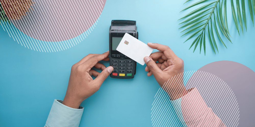 Mãos masculinas aproximando cartão de uma maquininha de cobranças repousada sobre um fundo azul claro