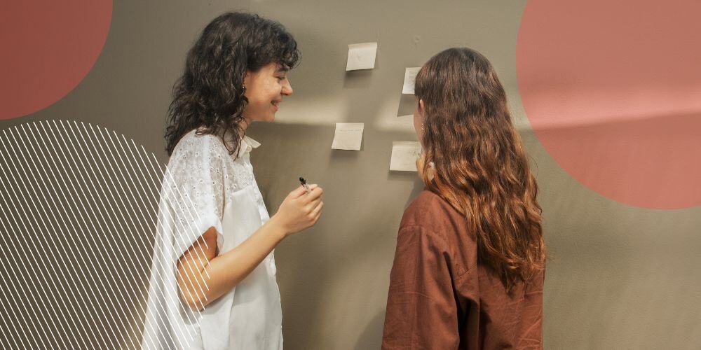 Colegas de trabalho organizando tarefas delegadas com post its colados em parede cinza