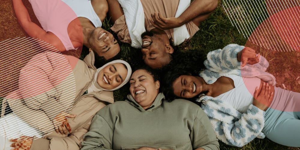 Grupo de pessoas diversas deitadas em grama enquanto sorriem para a foto